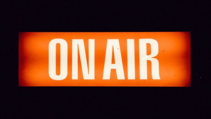 a neon orange sign with text that reads "On Air" against a black background