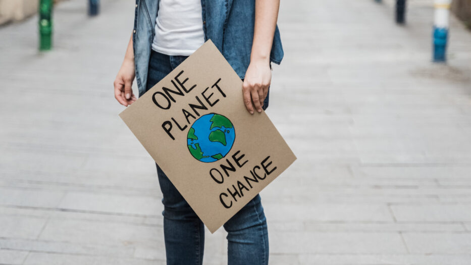 A young person holding a climate change awareness sign saying, “One planet, one chance.”